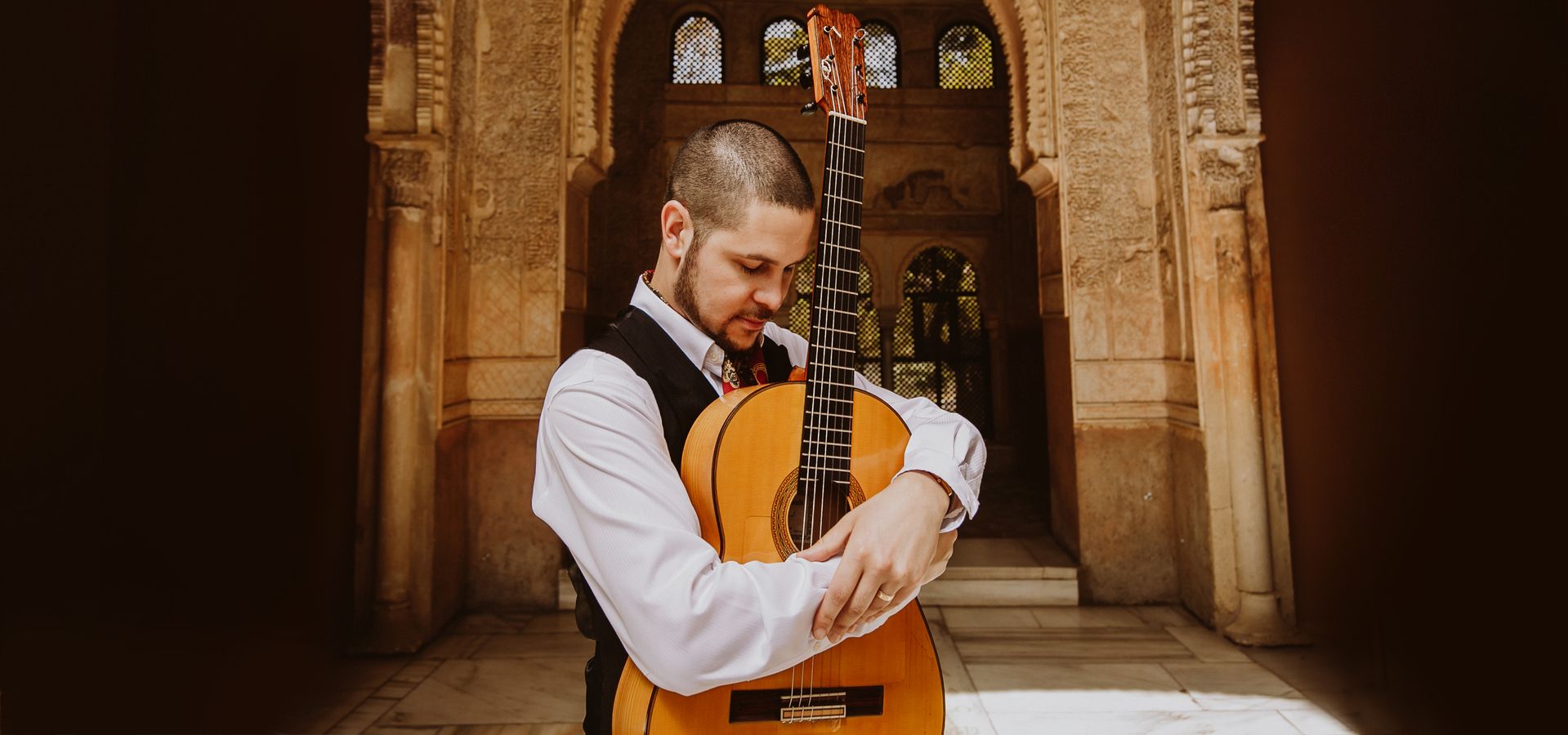 Samuel Moore stood in front of an archway with his guitar
