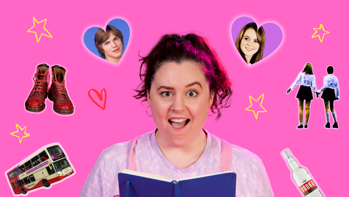 A photo of Beth (a white person with dark hair in a high ponytail, wearing pink dungarees and a lilac tie-dyed t-shirt). Beth is against a pink backdrop, opening a blue diary with a scandalised expression - one eyebrow raised, mouth open in shocked amusement. 
