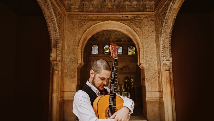 Samuel Moore stood in front of an archway with his guitar