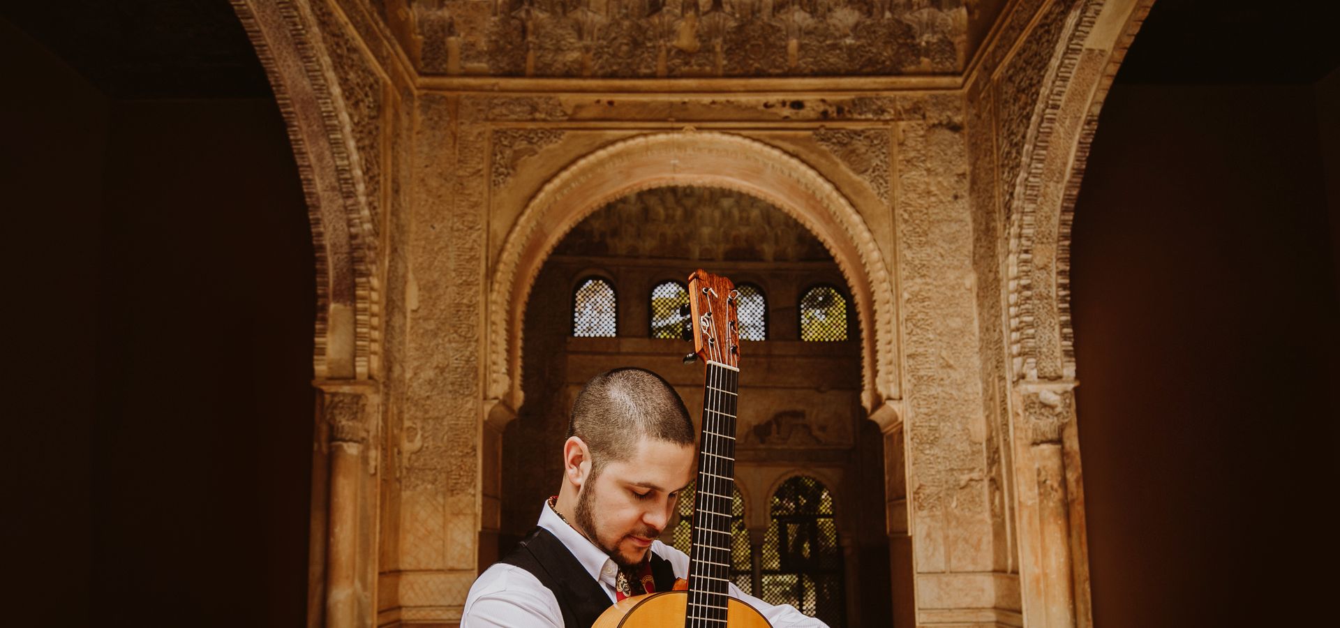 Samuel Moore stood in front of an archway with his guitar