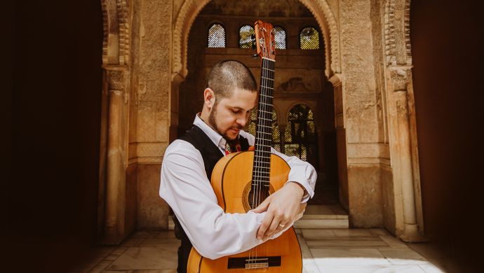 Samuel Moore stood in front of an archway with his guitar